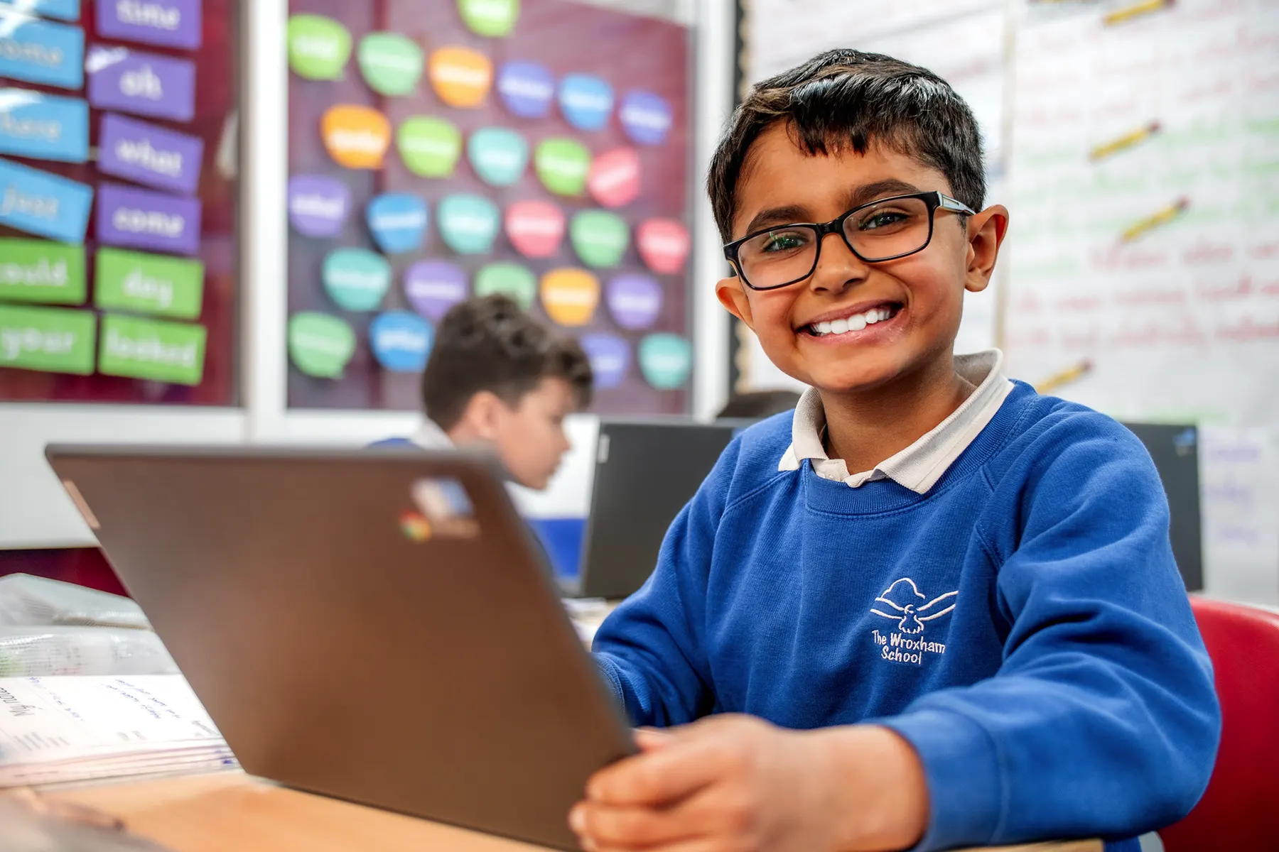 A boy on a laptop in class smiling